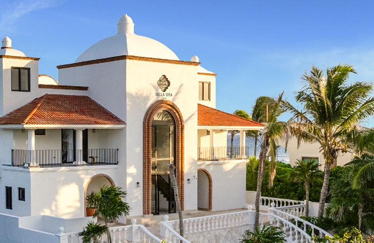 Exterior facade of Bella Vita Tulum luxury beachfront villa with white stucco architecture and palm trees, Tankah Bay