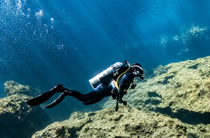 Scuba diver exploring underwater rock formations in the crystal clear waters of Tulum Mexico