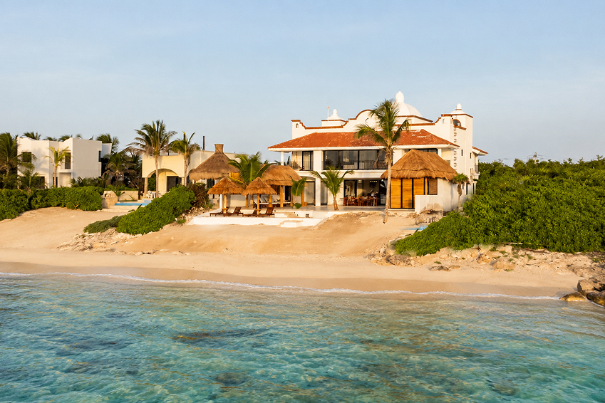 Beachfront villa at Bella Vita Tulum with palapa lounges, clear turquoise water, and sandy shoreline